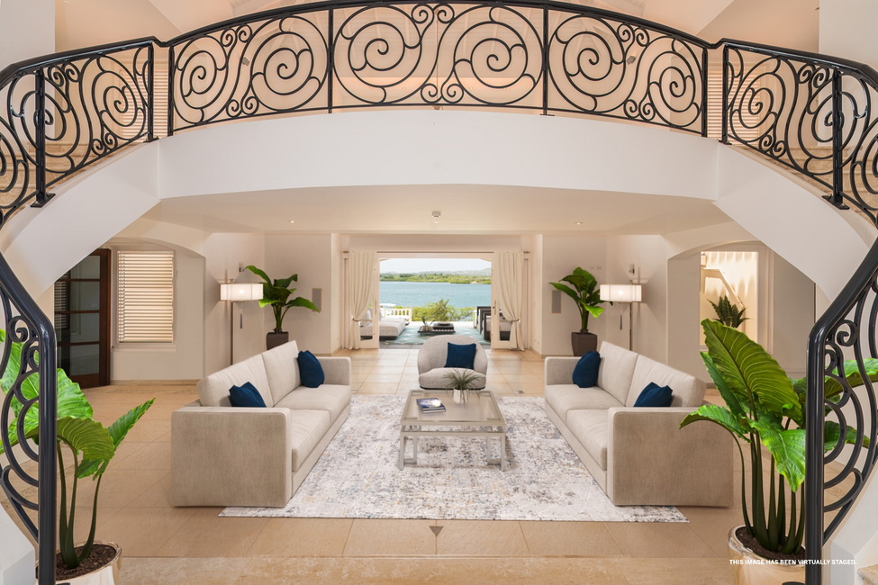 The foyer with double winding staircase, two story living room and waterview in the background, virtually staged.